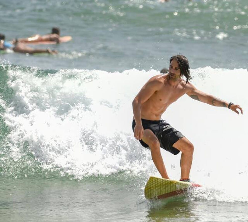 vivir en Nueva Zelanda chico moreno con el pelo largo surfeando en una playa